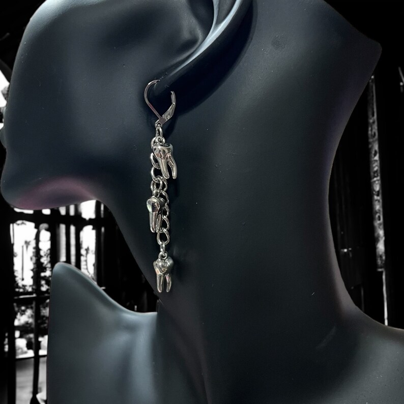 May include: Silver dangle earrings with a chain and multiple tooth charms.