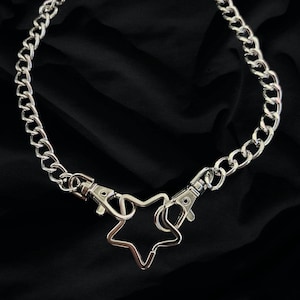 Op de afbeelding: Een zilveren ketting met een stervormige hanger en twee sluitingen.