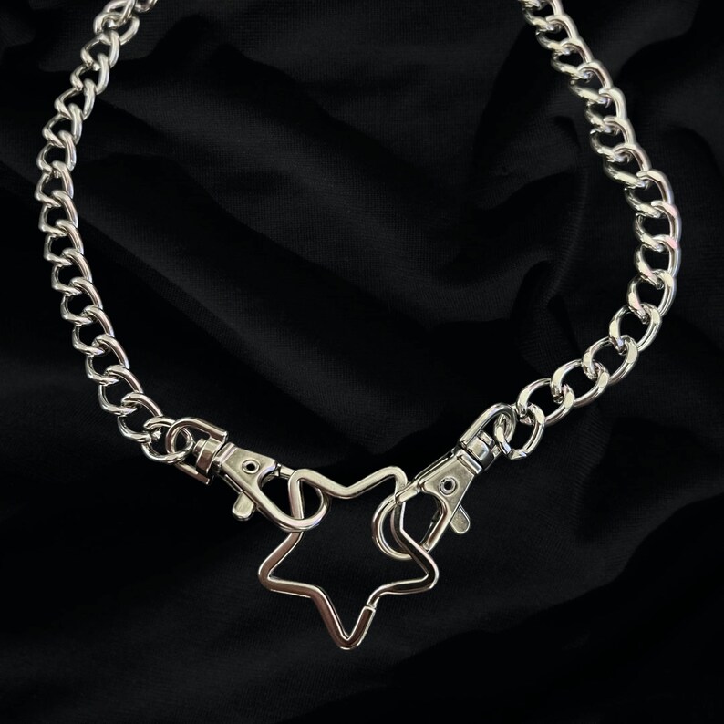 Op de afbeelding: Een zilveren ketting met een stervormige hanger en twee sluitingen.