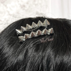 Pu&ograve; includere: Due fermagli per capelli argentati con punte appuntite. I fermagli hanno la forma di una fila di punte.