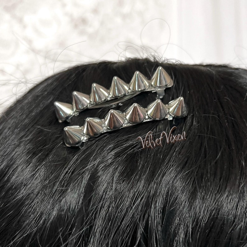 Pu&ograve; includere: Due fermagli per capelli argentati con punte appuntite. I fermagli hanno la forma di una fila di punte.