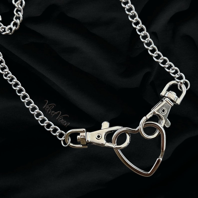 May include: A silver chain necklace with a heart-shaped clasp. The chain is made of thick, linked metal and the clasp is a heart shape with a hook.