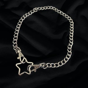 Op de afbeelding: Een zilveren ketting met een stervormige hanger. De ketting is gemaakt van metalen schakels en heeft een karabijnhaak.
