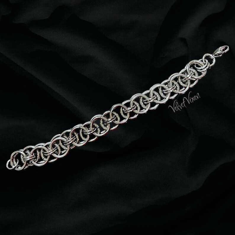Pode incluir: Uma pulseira de malha de corrente prateada com uma s&eacute;rie de an&eacute;is interligados. A pulseira &eacute; exibida em um fundo preto. O texto "Velvet Vixen" &eacute; vis&iacute;vel na pulseira.