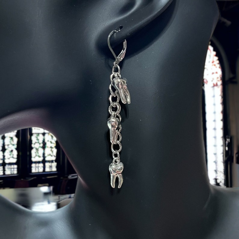 May include: Silver dangle earrings with a chain and three tooth charms.