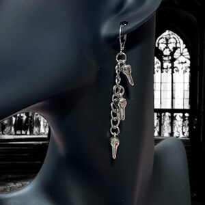 May include: Silver dangle earrings with a chain and three skull charms.