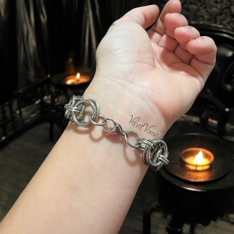 Pode incluir: Uma pulseira prateada com uma s&eacute;rie de an&eacute;is interligados e elos de corrente. A pulseira &eacute; presa com um fecho lagosta. O texto "Velvet Vixen" &eacute; vis&iacute;vel no pulso.
