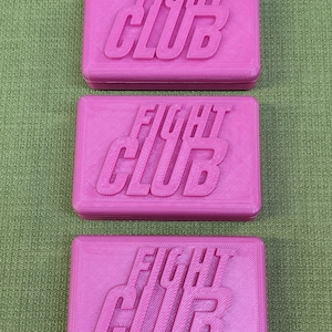May include: Three rectangular pink bars with the words FIGHT CLUB embossed in raised lettering on the top surface. Each bar features a smooth, uniform finish and a consistent, bold pink color throughout the entire rectangular structure.