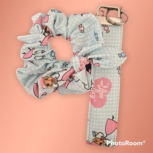 May include: A blue and pink patterned scrunchie and key chain set. The scrunchie has a bow and the keychain has a heart with the text "I love you".