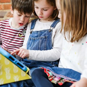 May include: Three children are sitting on a brick step, looking at a tablet computer in a yellow pineapple-patterned case. The tablet is blue and has a white case.