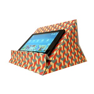 May include: A red, yellow, and blue geometric patterned cardboard stand for a tablet. The stand is folded into a triangular shape and has a slot to hold the tablet in place. A tablet with a blue screen is in the stand.