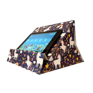 May include: A tablet stand made of cardboard with a unicorn and rainbow design. The stand is folded into a triangle shape and has a slot for a tablet. The tablet is showing a screen with a variety of apps.