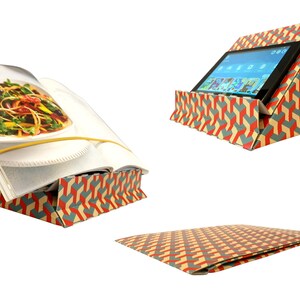 K&ouml;nnte beinhalten: Ein faltbarer St&auml;nder aus Pappe mit einem geometrischen Muster in Rot, Gelb und Blau. Der St&auml;nder kann verwendet werden, um ein Buch oder ein Tablet zu halten.