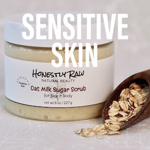 May include: A white jar of HonestLy Raw Oat Milk Sugar Scrub for face and body. The jar is labeled "Sensitive Skin" and "Approved Sensitive Skin". The jar is sitting on a white surface with a wooden scoop filled with oats.