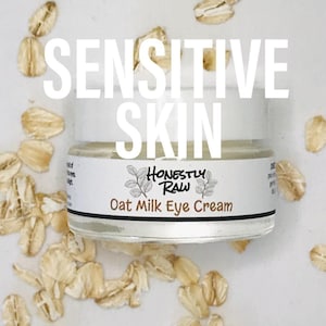 May include: A white jar of oat milk eye cream with the text "Honestly Raw" and "Oat Milk Eye Cream" on the label. The jar is surrounded by oat flakes on a white background. The text "Sensitive Skin" is written in large letters above the jar.