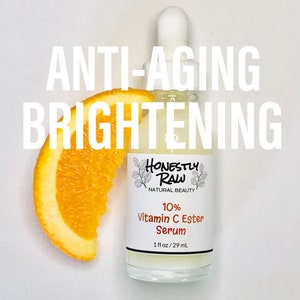 May include: A clear glass bottle with a white dropper top and a white label. The label says "Honestly Raw Natural Beauty 10% Vitamin C Ester Serum 1 fl oz/29 mL". The bottle is sitting on a white surface with a slice of orange next to it. The text "ANTI-AGING BRIGHTENING" is written in large white letters above the bottle.