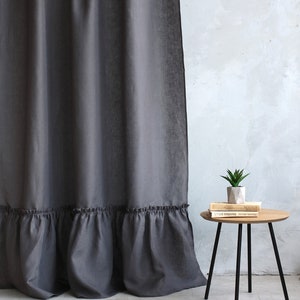 Puede incluir: Una cortina de lino gris antracita con un dobladillo con volantes. La cortina est&aacute; colgada delante de una pared blanca. Una peque&ntilde;a mesa de madera con patas negras est&aacute; en primer plano. La mesa tiene una peque&ntilde;a planta en maceta y dos libros en la parte superior.