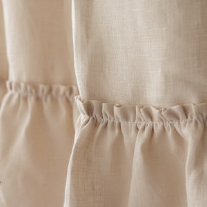 Puede incluir: Primer plano de una cortina de lino beige con un dobladillo con volantes. La tela es suave y texturizada, creando un aspecto delicado y rom&aacute;ntico.