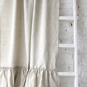 Puede incluir: Un par de cortinas de lino beige con un borde inferior con volantes. Las cortinas est&aacute;n colgadas frente a una pared de ladrillo blanco con una escalera de madera blanca apoyada en ella.