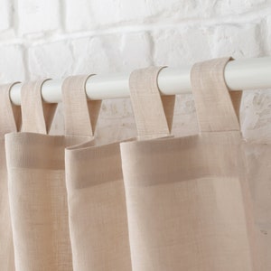 Puede incluir: Un juego de cortinas de lino beige colgadas de una barra blanca. Las cortinas est&aacute;n fruncidas en la parte superior y tienen un dise&ntilde;o simple y elegante.