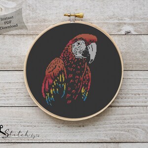 May include: Cross stitch pattern of a red, yellow, and blue macaw on a black background. The pattern is in a hoop and ready to be stitched.