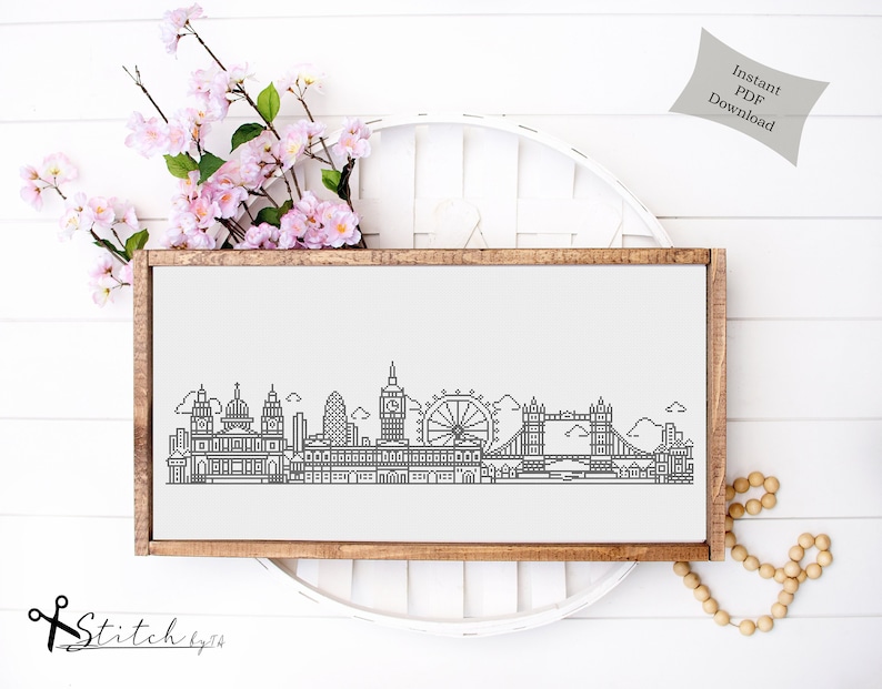 May include: A black and white line art illustration of the London skyline, including Big Ben, the London Eye, and Tower Bridge. The illustration is framed in a brown wooden frame and is displayed on a white surface.