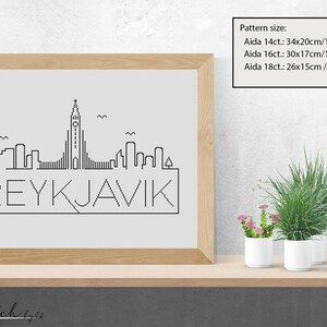 K&ouml;nnte beinhalten: Eine Schwarzwei&szlig;-Zeichnung der Skyline von Reykjavik mit dem Text "REYKJAVIK" darunter. Das Bild ist gerahmt und auf einem Regal mit zwei Topfpflanzen ausgestellt.
