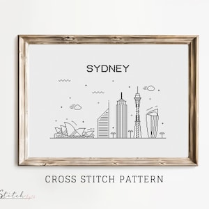 May include: A black and white cross stitch pattern of the Sydney skyline, featuring the Sydney Opera House, the Sydney Harbour Bridge, and the Sydney Tower. The pattern is framed in a light brown wood frame and includes the text "Sydney" and "Cross Stitch Pattern".