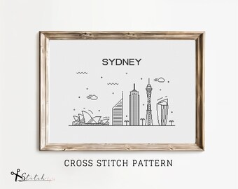 Peut inclure: Un motif de point de croix noir et blanc du ciel de Sydney, mettant en vedette l'opéra de Sydney, le pont du port de Sydney et la tour de Sydney. Le motif est encadré dans un cadre en bois brun clair et comprend le texte "Sydney" et "Point de croix".