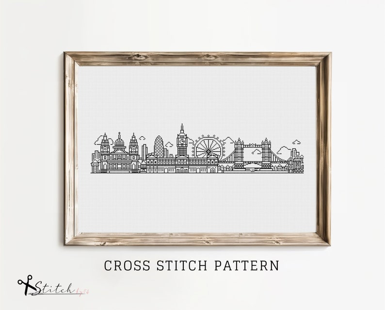 May include: Black and white line art cross stitch pattern of the London skyline, including Big Ben, the London Eye, and Tower Bridge. The pattern is framed in a light wood frame and displayed on a white wall. The text "CROSS STITCH PATTERN" is below the frame.