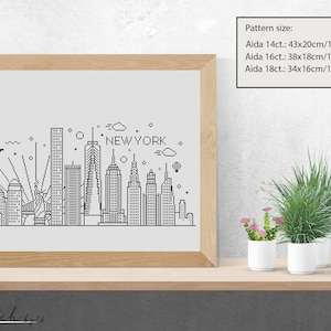 May include: A black and white line art illustration of the New York City skyline, including the Empire State Building, the Chrysler Building, and the Statue of Liberty. The text "NEW YORK" is written above the skyline. The image is framed and displayed on a shelf with potted plants.
