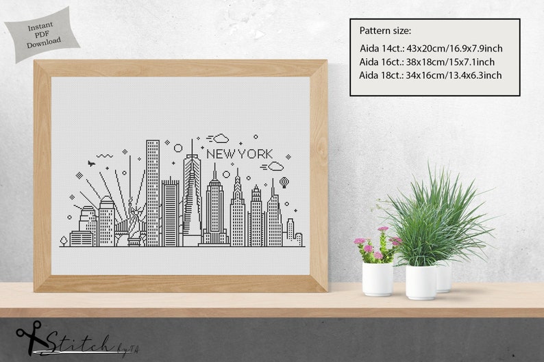 May include: A black and white line art illustration of the New York City skyline, including the Empire State Building, the Chrysler Building, and the Statue of Liberty. The text "NEW YORK" is written above the skyline. The image is framed and displayed on a shelf with potted plants.