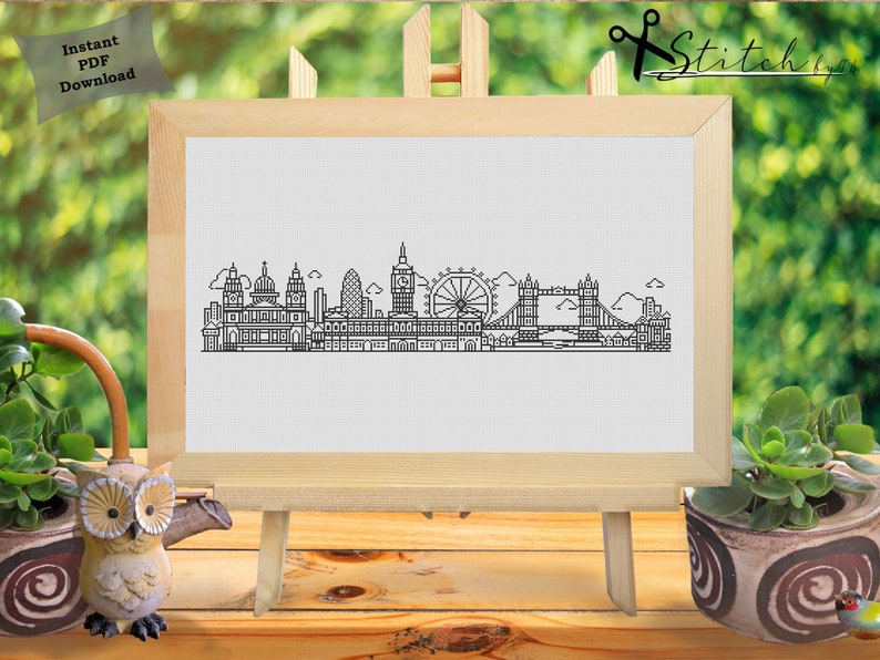 May include: Black and white line art illustration of the London skyline, including Big Ben, the London Eye, and Tower Bridge. The illustration is on a white background and framed in a wooden frame.