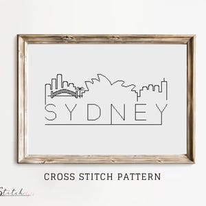 Op de afbeelding: Zwart-witte kruissteekpatroon van de skyline van Sydney, inclusief het Sydney Opera House en de Harbour Bridge. Het woord "SYDNEY" is onder de skyline gestikt.