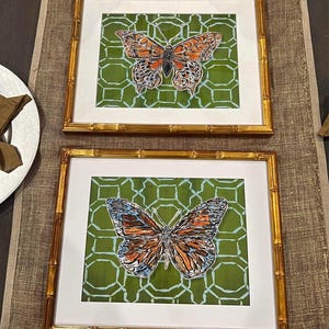 May include: Two framed prints with a gold bamboo frame. Each print features a butterfly with orange, black, and blue wings on a green background with a geometric pattern.