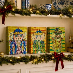 May include: Three rectangular canvas paintings featuring stylized nutcracker figures in vibrant, textured brushstrokes. The left painting shows a blue and gold nutcracker, the center a gold and green one, and the right a green and gold figure.