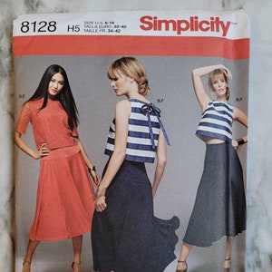 May include: Simplicity sewing pattern 8128 features three women modeling different outfits. The pattern includes a top with a bow, a skirt, and a lace top. The size range is U.S. 6-14. The pattern is designed and printed in the USA.