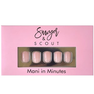 May include: A pink box of Sawyer & Scout press-on nails. The box has a rectangular window displaying five oval-shaped nails with a light pink ombre design. The text "Mani in Minutes" is printed on the box.