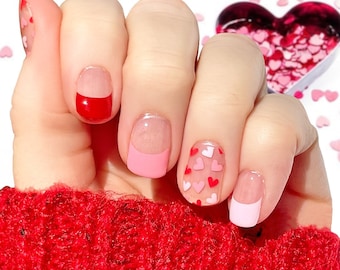 May include: Close-up of a hand with pink and red nail polish. The nails are decorated with small pink and red hearts.