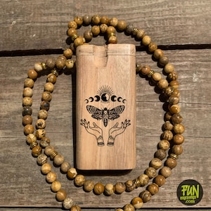 May include: A light brown wooden box with a carved moth and moon phase design, resting on a wooden surface. A beaded necklace with brown and gold beads surrounds the box. The box has the text "FUN engravings .com".