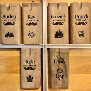 May include: Six wooden boxes with engraved designs and names. The boxes are arranged in two rows of three. The top row has the names Burley, Kev, Graeme, and Pnark. The bottom row has the names Kyle and Leon. Each box has a different design, including a mustache, trees, musical notes, a rose, and a maple leaf.
