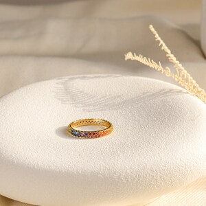 Könnte beinhalten: Ein goldener Ring mit einem Band, das mit bunten Steinen besetzt ist, die einen Regenbogen bilden.