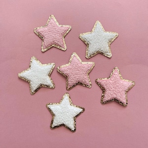 May include: Six sparkly gold-trimmed stars on a pink background. Three stars are pink and three are white.