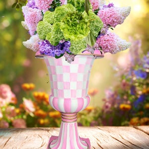 May include: A decorative vase filled with a vibrant floral arrangement. The vase features a pink and white checkered pattern on the upper portion and pink and white stripes on the base. The flowers include pink, purple, and green blooms, creating a colorful display.
