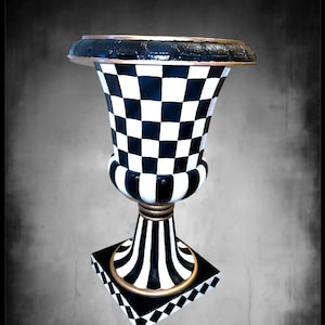 May include: A black and white checkered ceramic vase with a gold trim. The vase has a wide base and a narrow neck.