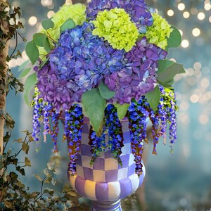 May include: A decorative violet and white urn planter filled with a vibrant floral arrangement. The arrangement includes purple, blue, and chartreuse flowers with cascading blue blossoms. The urn has a checkered pattern and is on a purple base. Text on the image reads "Violet Purple Urn Planter."
