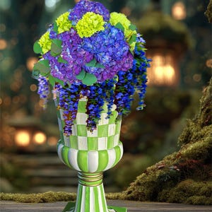 May include: A decorative urn with a green and white checkered and striped design, holding a vibrant bouquet of purple, blue, and yellow flowers. The urn sits on a square base with a gold trim.