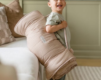 Peut inclure: Un tapis de sieste matelassé à motif vichy beige et blanc avec des sangles de transport intégrées. Le tapis rectangulaire présente une texture douce et rembourrée ainsi qu'une petite étiquette rectangulaire sur la surface avant.