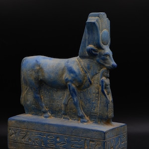 May include: A blue lapis lazuli statue of the Egyptian goddess Hathor, depicted as a cow with a sun disk and horns. The statue is standing on a base with hieroglyphs.