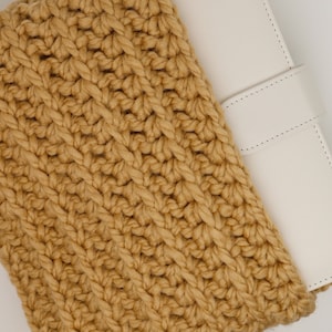 May include: A close-up of a brown crocheted pouch with a white leather notebook inside.
